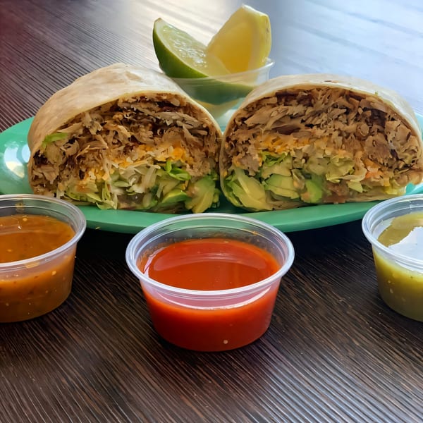 Two Chilitos Mexican Grill burritos, cut in half, with three salsa cups and lime wedges.