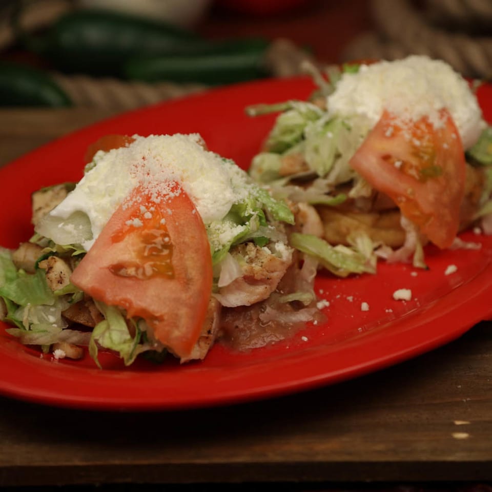 Two Chilitos Mexican Grill tostadas with chicken, lettuce, tomato, sour cream, and cheese on a red plate.