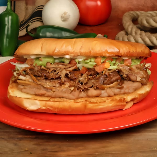 Chilitos Mexican Grill's torta with shredded meat, beans, lettuce, tomato, and guacamole on a red plate.